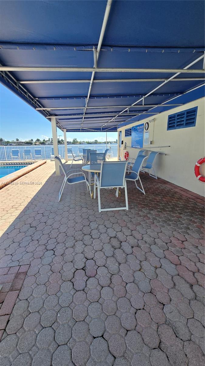 Covered outdoor patio featuring concrete paver flooring, a retractable fabric awning, and perimeter metal fencing