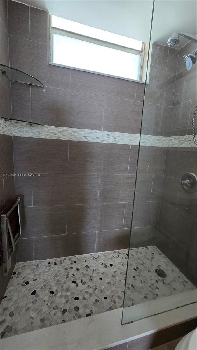 Walk-in shower featuring large-format wall tile, a horizontal decorative mosaic tile accent, pebble-style floor tiling, a glass enclosure, and a transom window