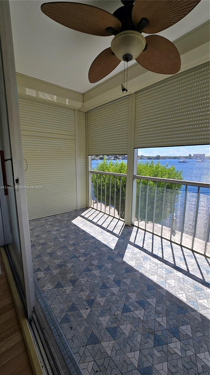 Covered balcony featuring patterned tile flooring, retractable privacy shutters, metal railings, and an integrated ceiling fan
