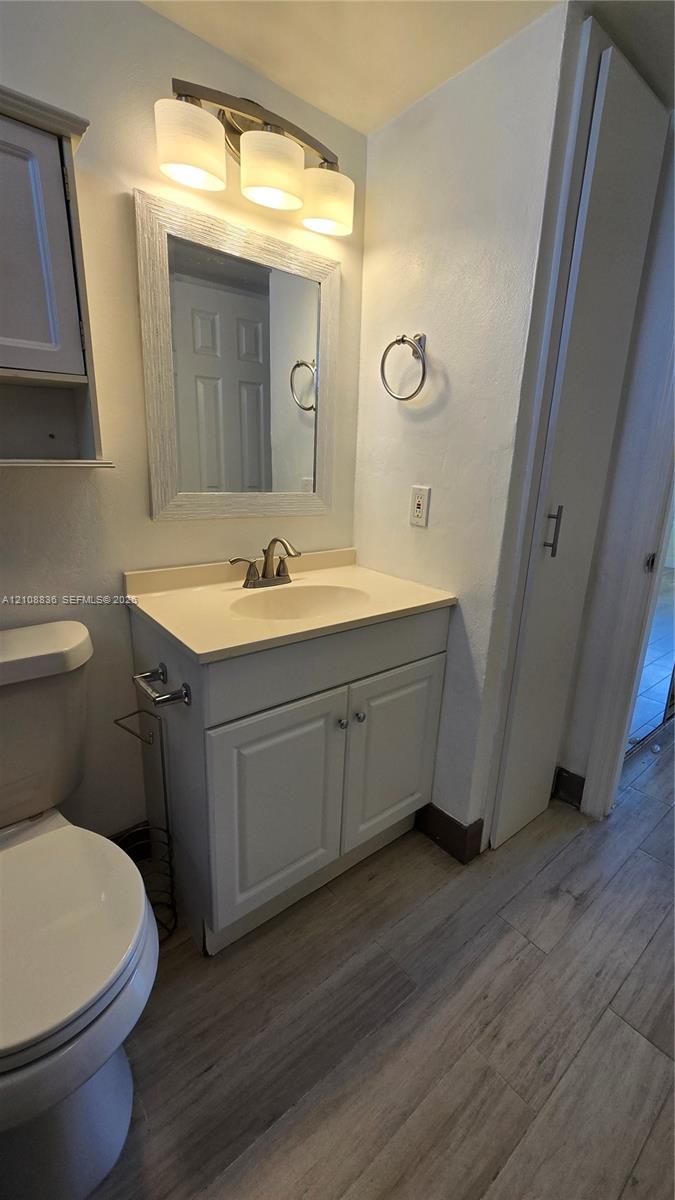 Bathroom featuring a vanity with shaker-style cabinetry, solid surface countertop, wood-finish flooring, and a three-light wall-mounted fixture