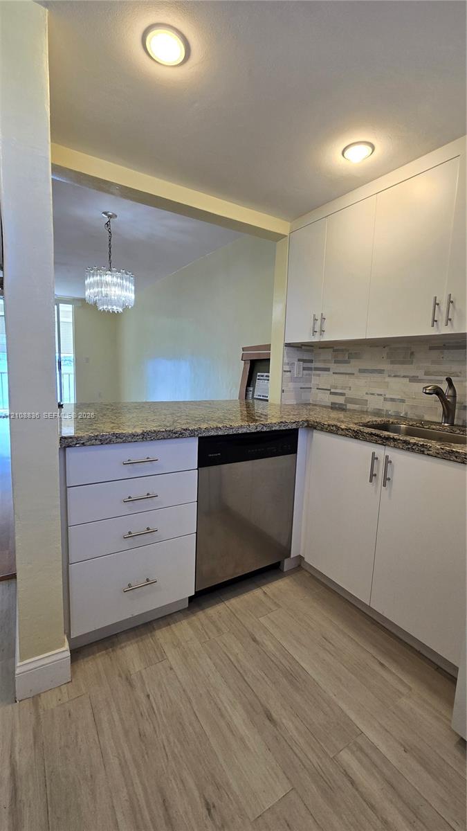 Kitchen featuring white cabinetry, stone-finish countertops, stainless steel dishwasher, decorative tile backsplash, and wood-finish flooring