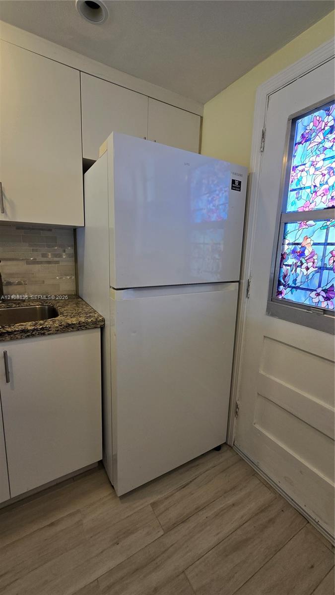 Kitchen area featuring white cabinetry, stone-finish countertops, wood-finish flooring, and a door with a decorative stained-glass insert