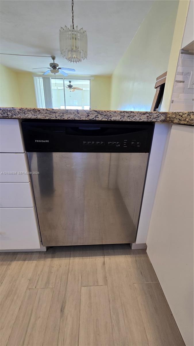 Stainless steel dishwasher, stone-finish countertop, white cabinetry, and wood-finish flooring