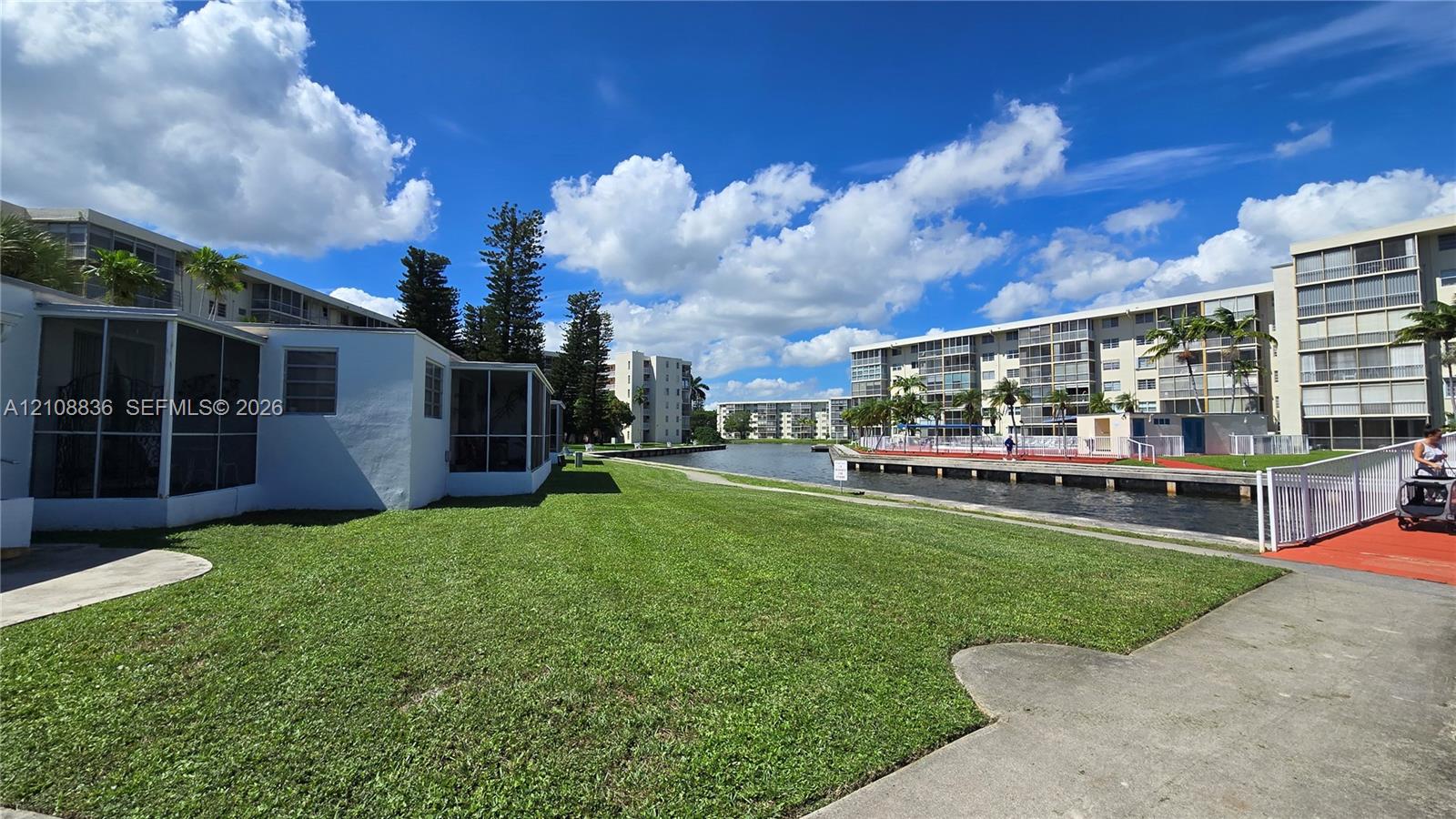 Ground-level exterior featuring screen-enclosed patios, expansive turf lawn, concrete walkways, and canal frontage