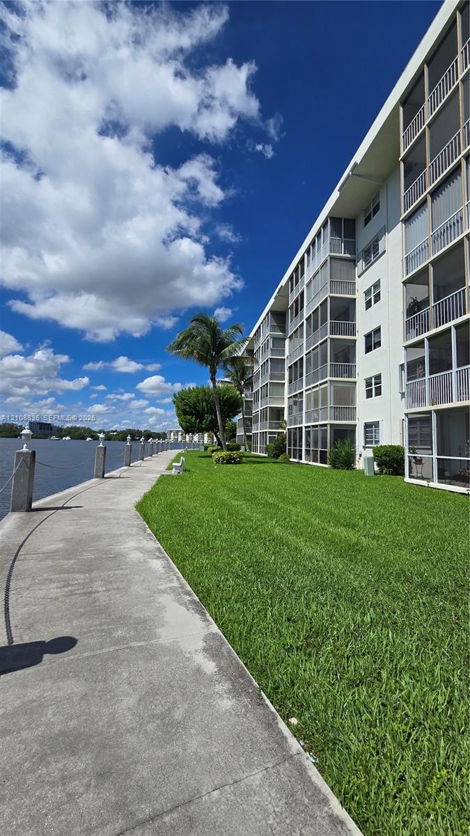 Concrete waterfront promenade featuring a metal-post rope railing, expansive manicured lawn, and multi-story building exterior with stacked screened balconies