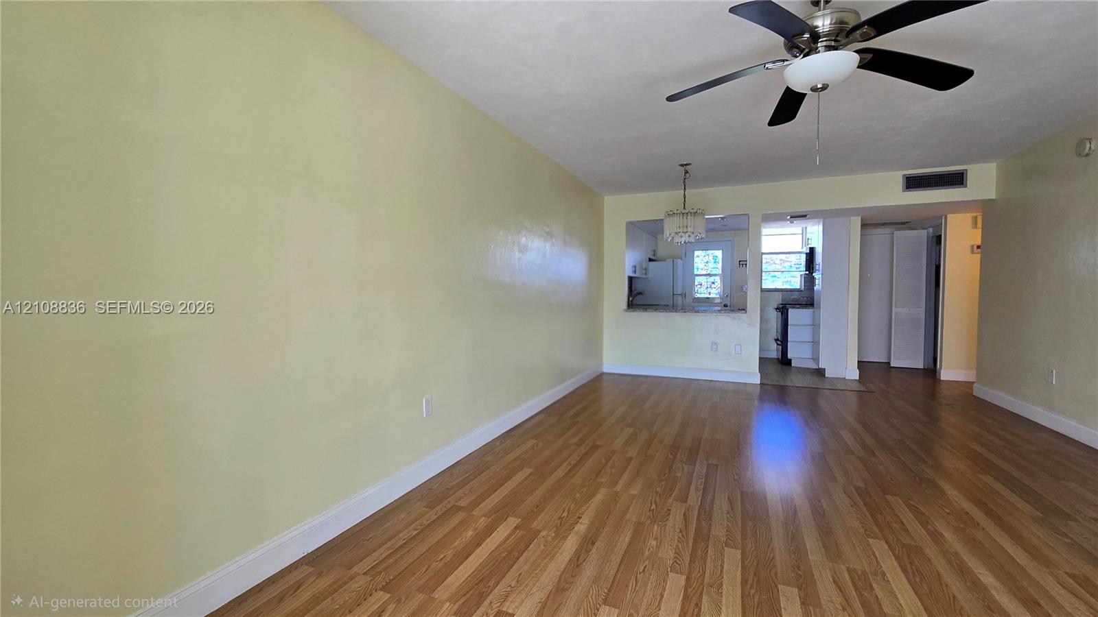 Open-concept interior featuring wood-finish flooring, a ceiling fan with integrated lighting, a decorative hanging pendant fixture, and a pass-through opening