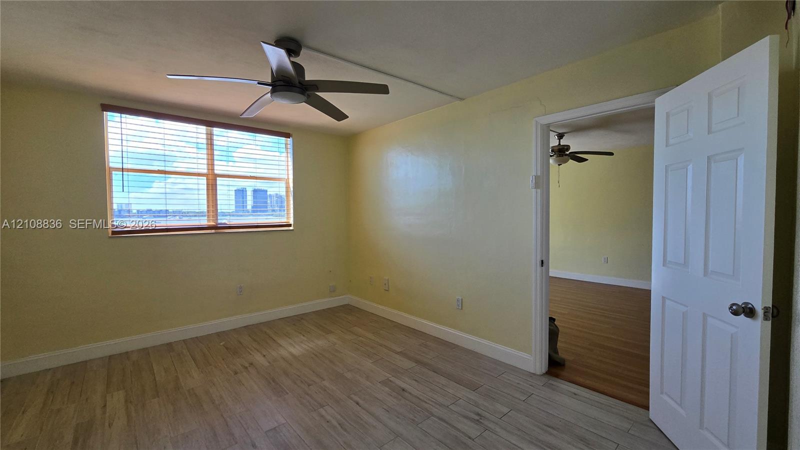 Room featuring light-toned wood-finish flooring, a multi-blade ceiling fan, and large horizontal window with slatted blinds