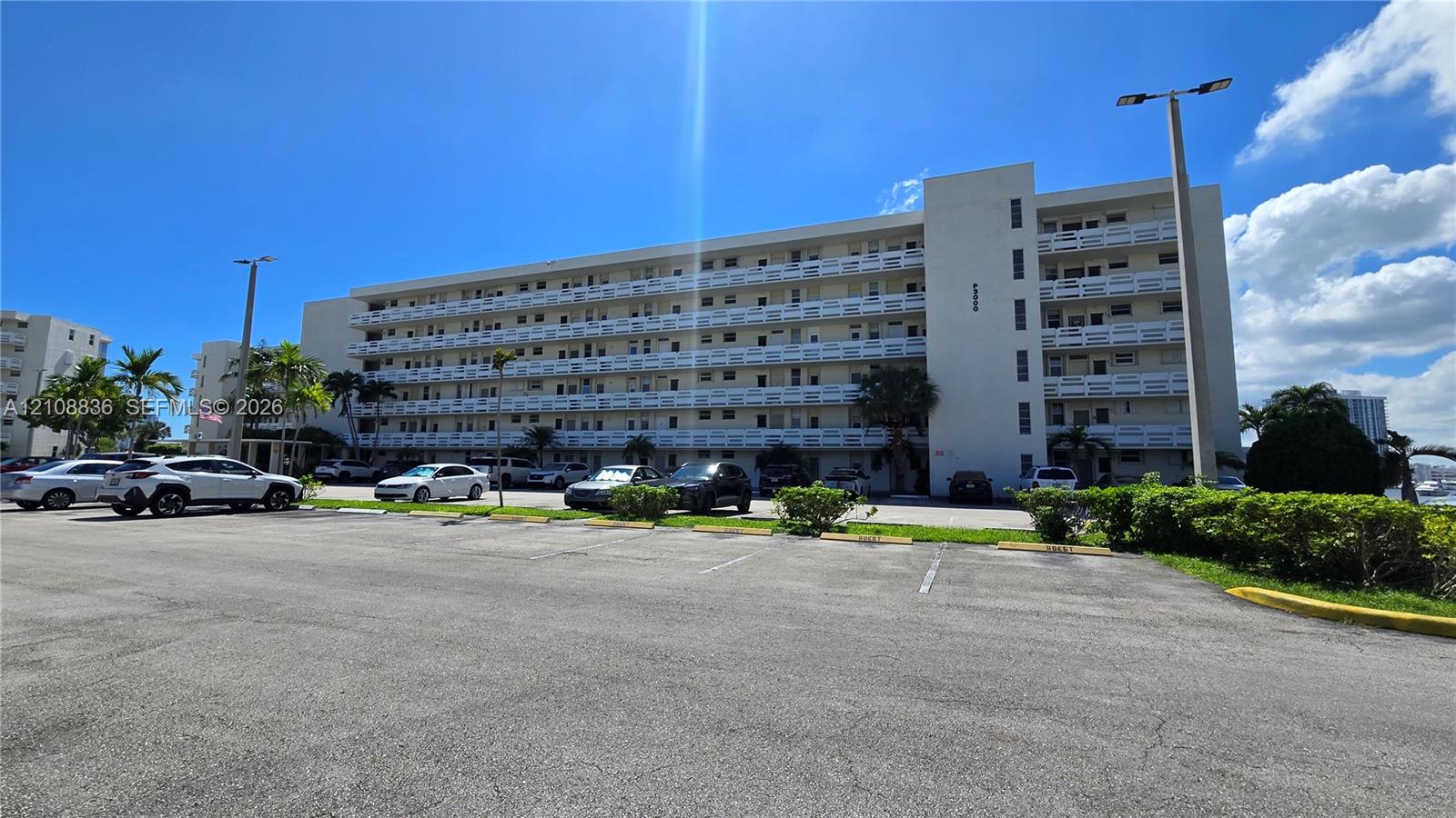 Mid-rise concrete exterior featuring uniform balcony railings and paved surface parking