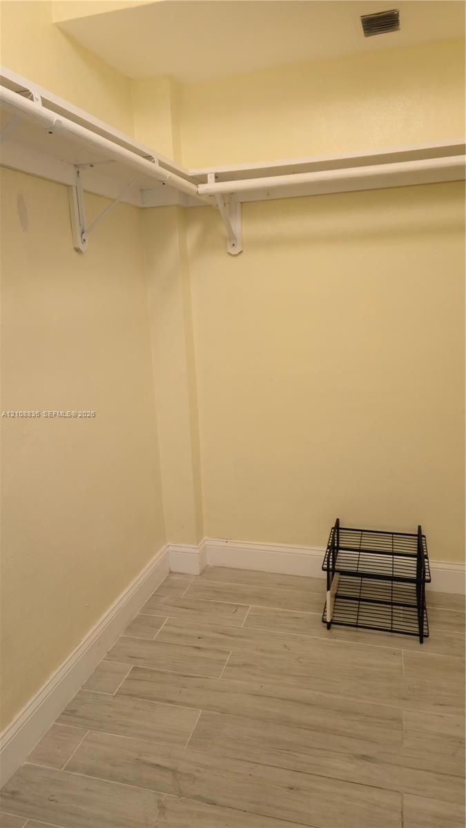 Walk-in storage area featuring wood-finish tile flooring and wraparound white shelving