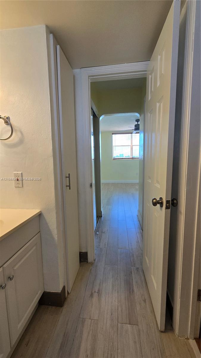Bathroom featuring a vanity with a countertop, integrated floor-to-ceiling cabinetry, and light-toned wood-finish flooring extending into the hallway