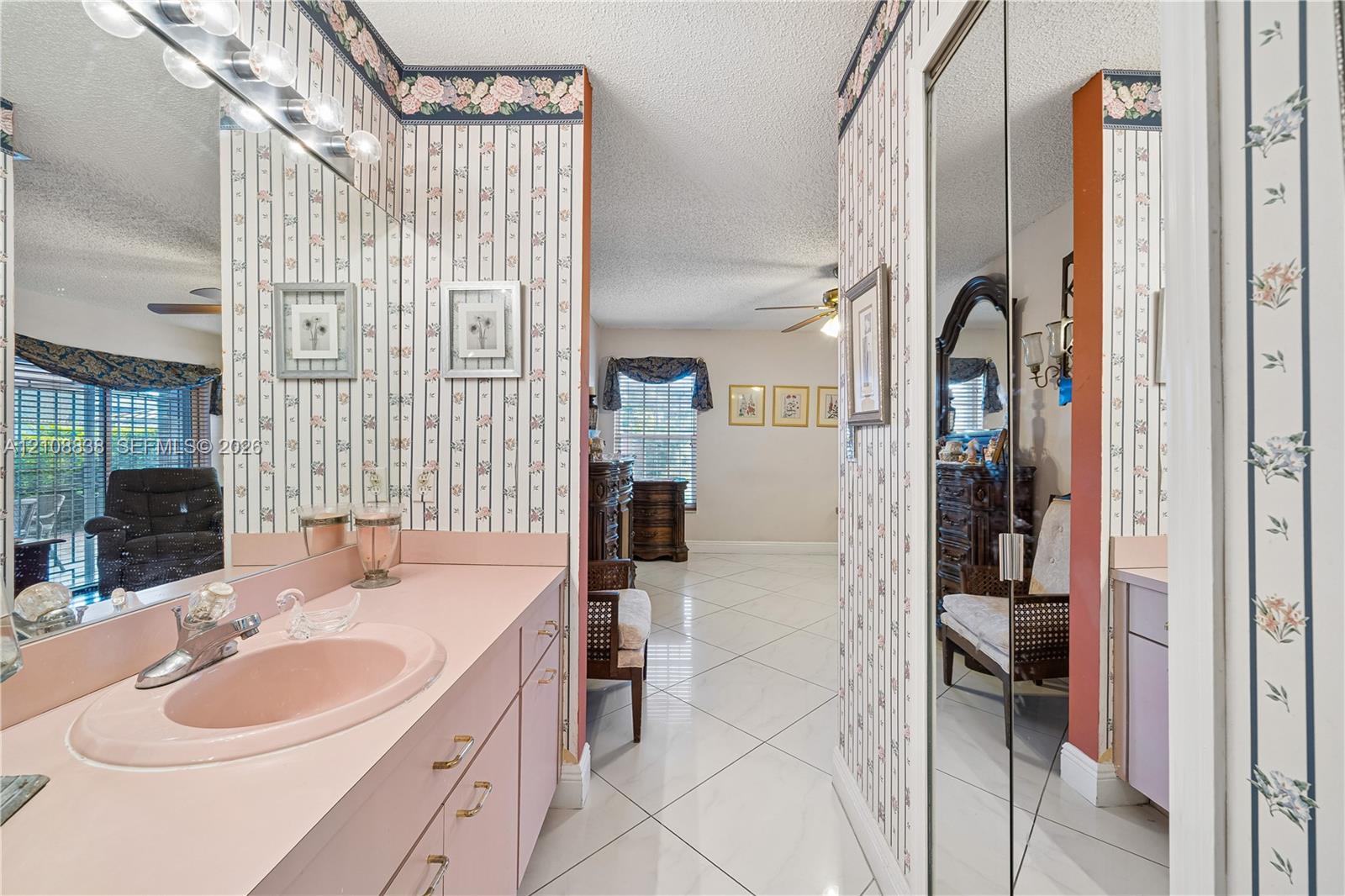 Bathroom featuring a vanity with a drop-in sink, expansive wall-to-wall mirror, built-in floor-to-ceiling mirrored closet doors, and ceramic tile flooring