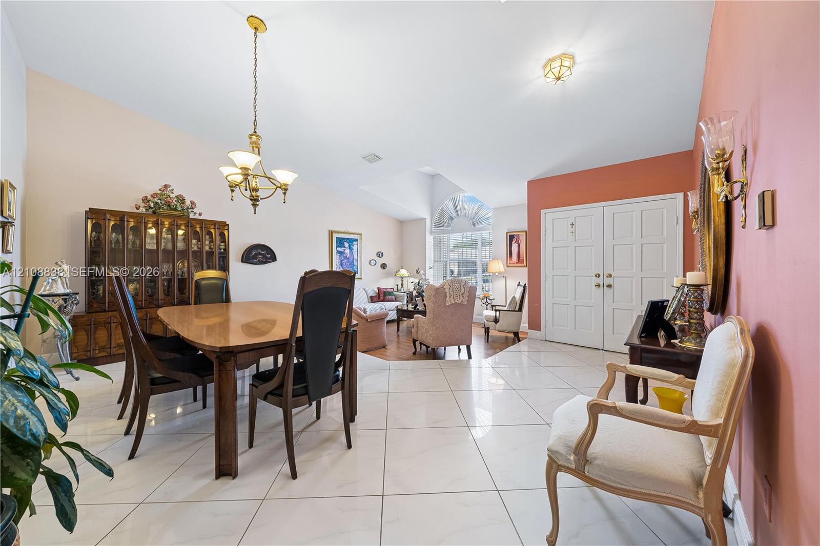 Open-concept living space featuring high vaulted ceilings, large-format tile flooring, a multi-light brass chandelier, and an arched window