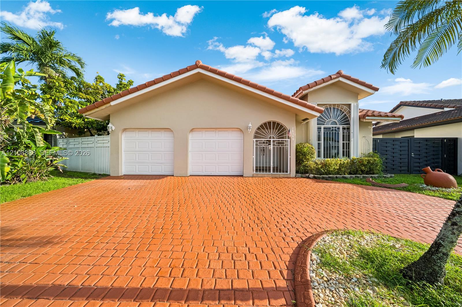 Single-story residence featuring a two-car garage, a stamped-pattern concrete driveway, an arched entryway with a decorative security gate, and an arched transom window