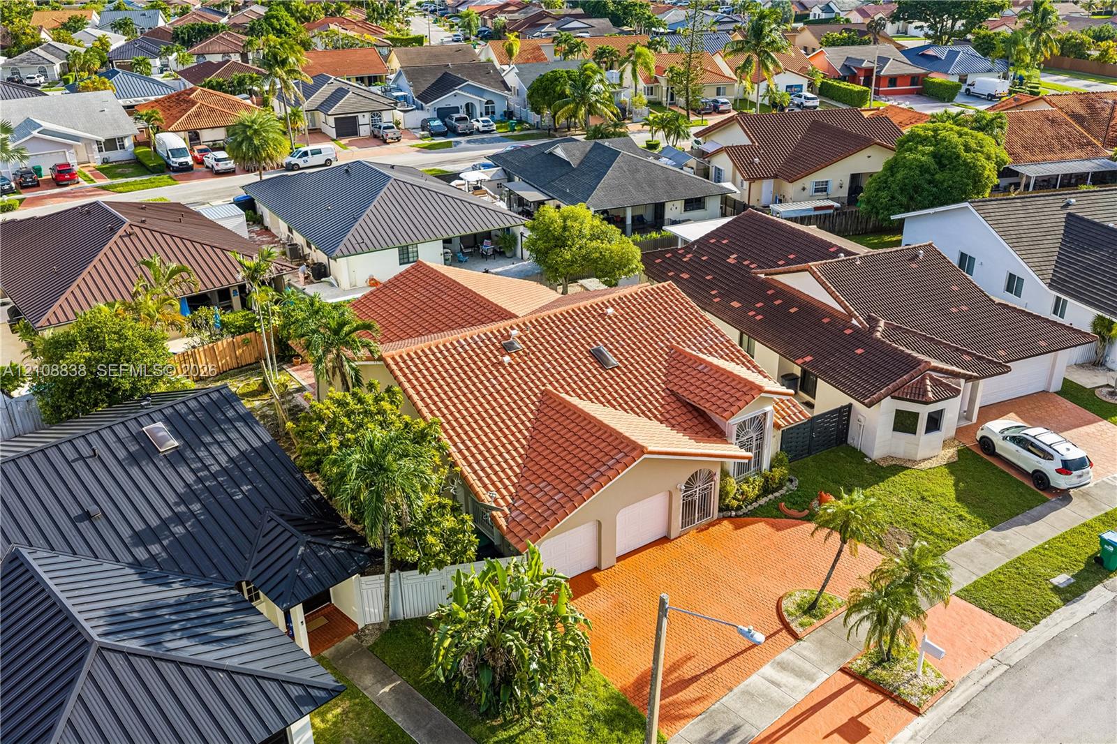 Residence featuring a terracotta-tile roof, two-car garage, and a paver-stone driveway, set within a residential neighborhood with mature landscaping and palm trees