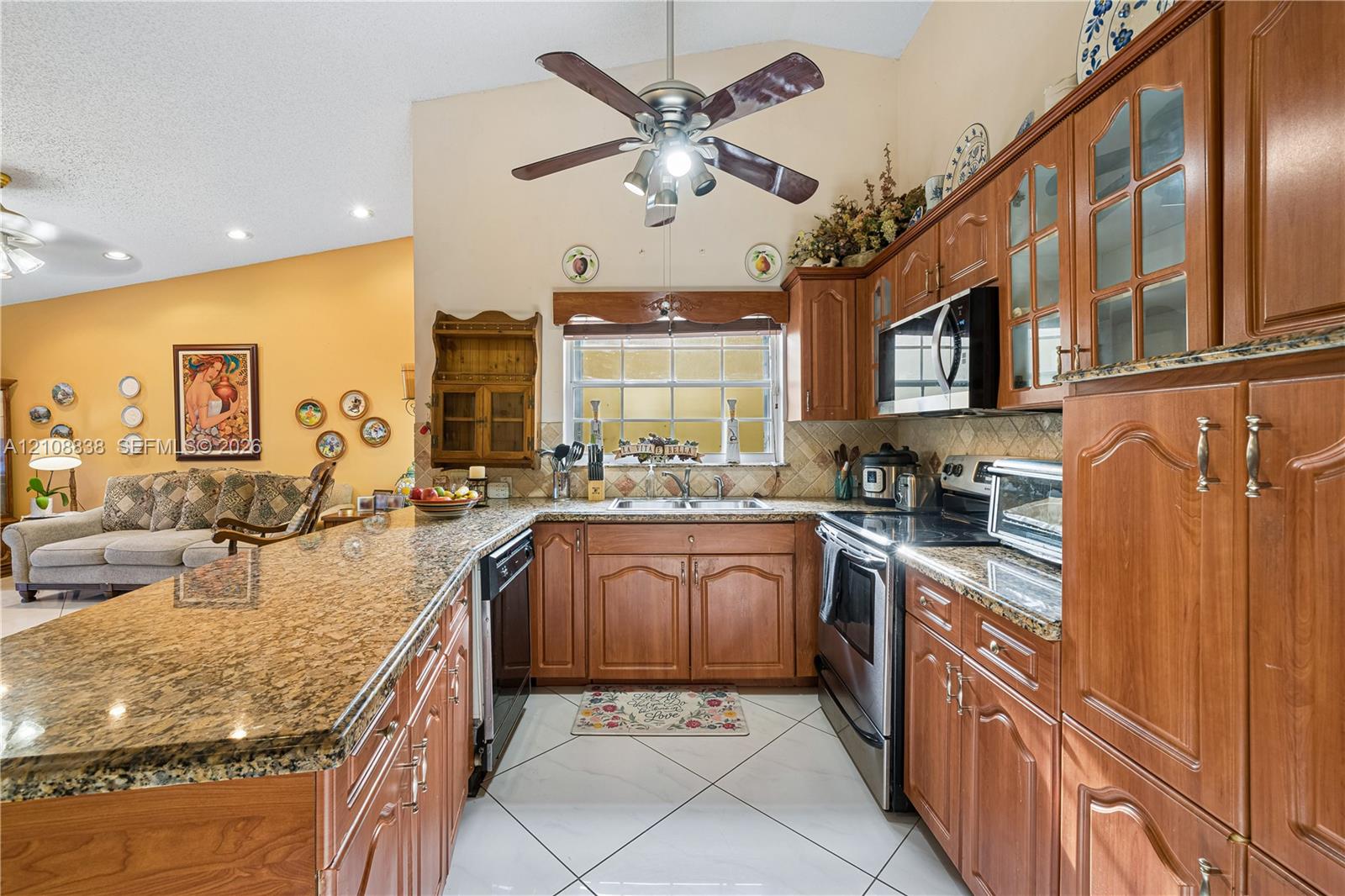 Kitchen featuring wood cabinetry, stone countertops, stainless steel appliances, tile flooring, and a ceiling fan