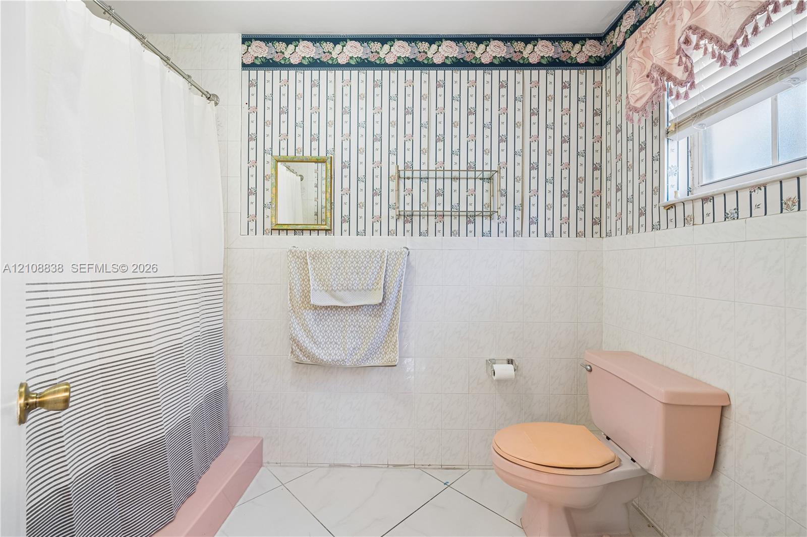 Bathroom featuring white tile wall cladding, patterned wallpaper, a built-in wall-mounted glass shelf, and a shower area with a raised platform