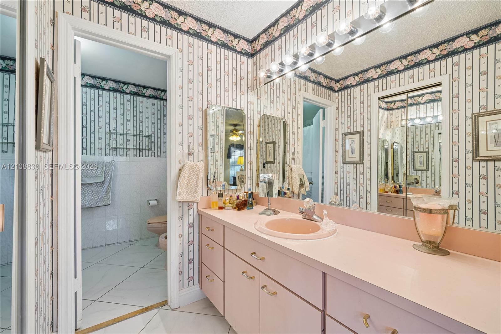 Built-in vanity featuring a solid-surface countertop with an integrated basin, multi-drawer cabinetry, large wall-mounted mirror, and multi-bulb lighting fixture
