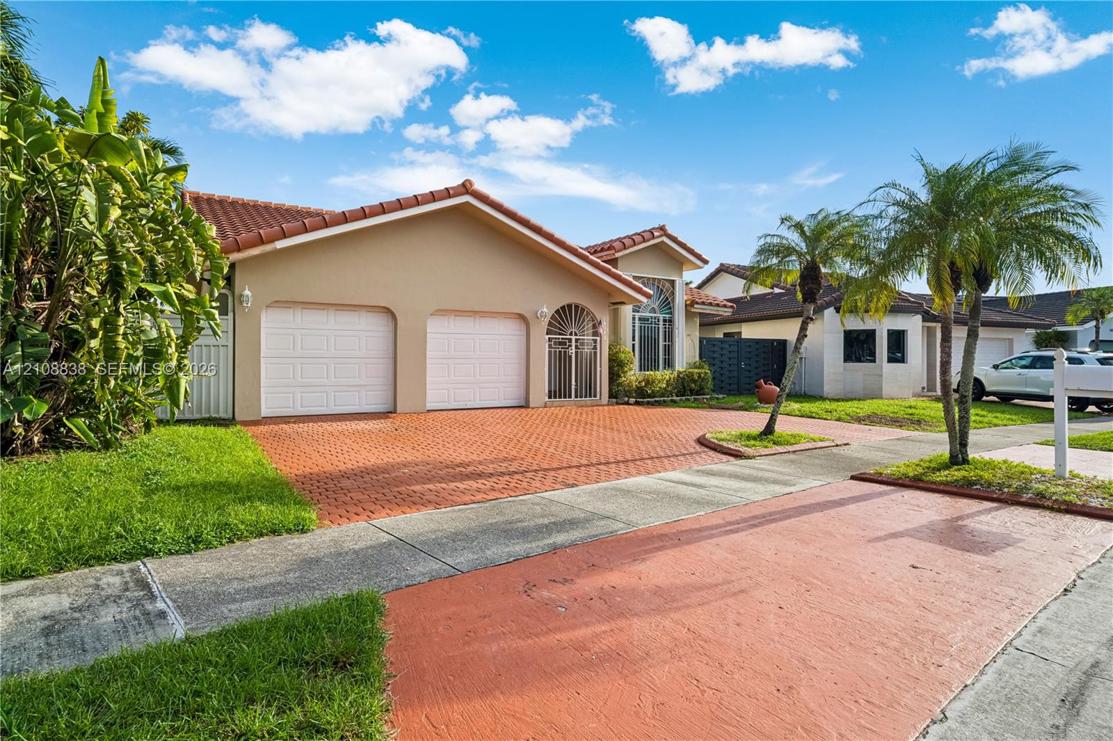 Single-story exterior featuring a clay tile roof, dual-bay garage, decorative arched entryway, and a paved brick driveway