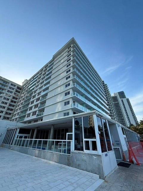 High-rise exterior featuring stacked balconies with glass railings, expansive floor-to-ceiling windows, and paved stone patio ground level