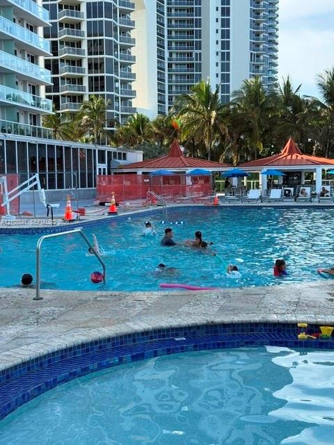 Outdoor swimming pool and spa featuring stone decking, blue tile trim, and multiple covered cabanas