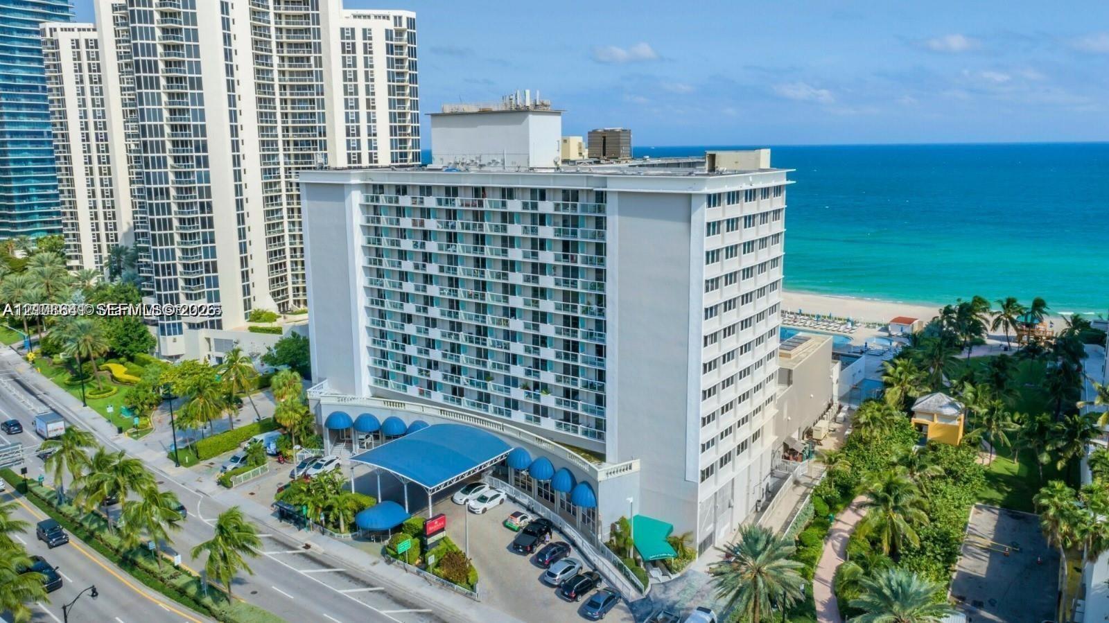High-rise building featuring private balconies, a covered porte-cochre entry with fabric awnings, and oceanfront positioning with direct coastal access