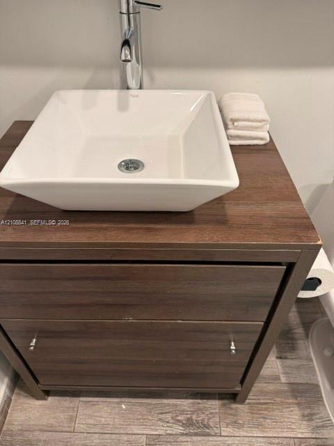 Vanity featuring a wood-finish cabinet with dual drawers, a square ceramic vessel sink, and a chrome single-handle faucet