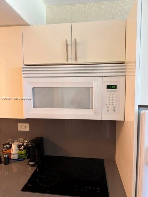 Built-in over-the-range microwave, flat-panel cabinetry with brushed-metal pulls, and a smooth-surface electric cooktop set into a solid-surface countertop
