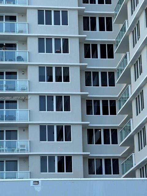 High-rise exterior featuring a light gray facade, multi-level balconies with glass railings, and expansive rectangular windows