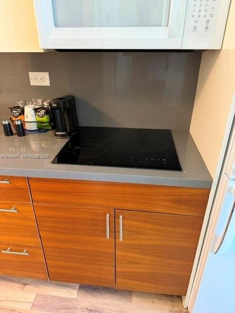 Kitchen area featuring a smooth-surface electric cooktop, solid-surface gray countertops, matching full-height backsplash, and wood-finish cabinetry with brushed metal hardware