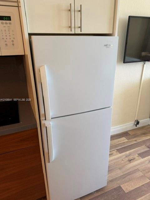 White top-freezer refrigerator, built-in cabinetry with silver-tone bar pulls, and wood-finish flooring