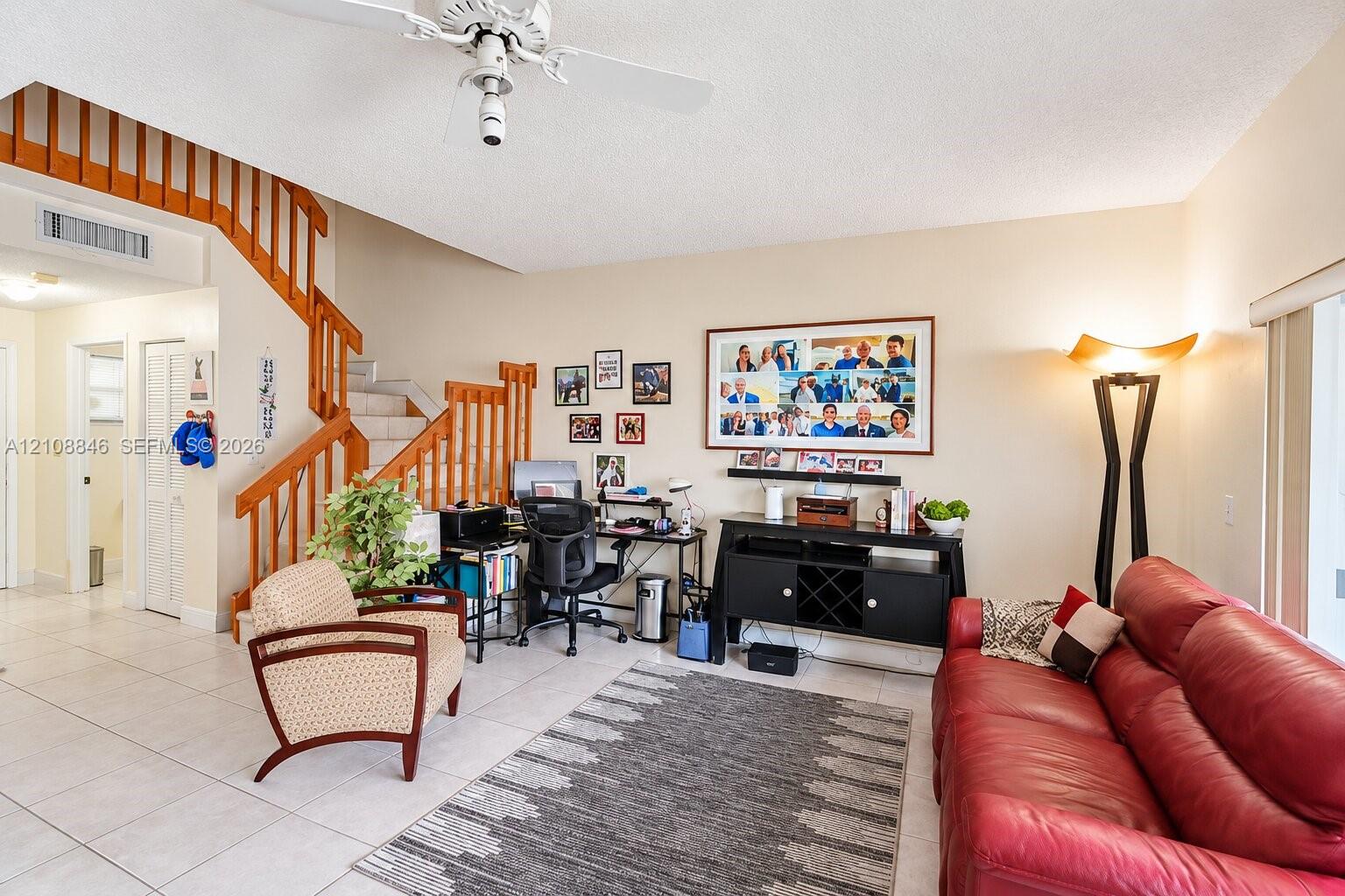 High-ceiling living area featuring tile flooring, a prominent staircase with wood railings, and a ceiling fan