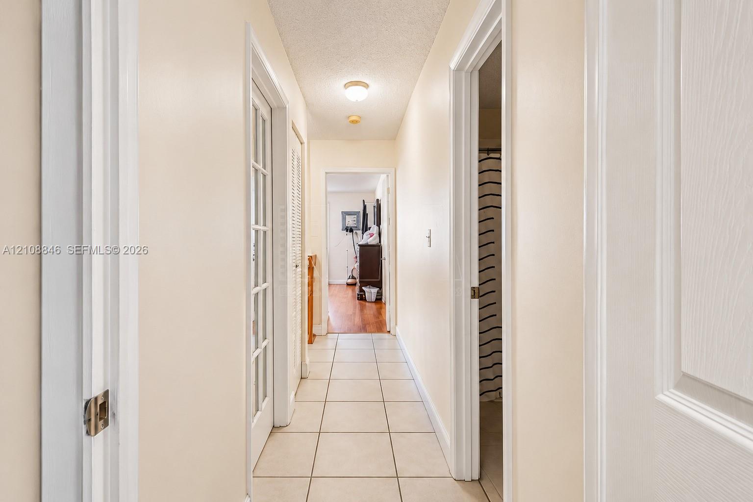 Hallway featuring ceramic tile flooring, a multi-pane glass door, louvered closet doors, and a flush-mount ceiling light fixture