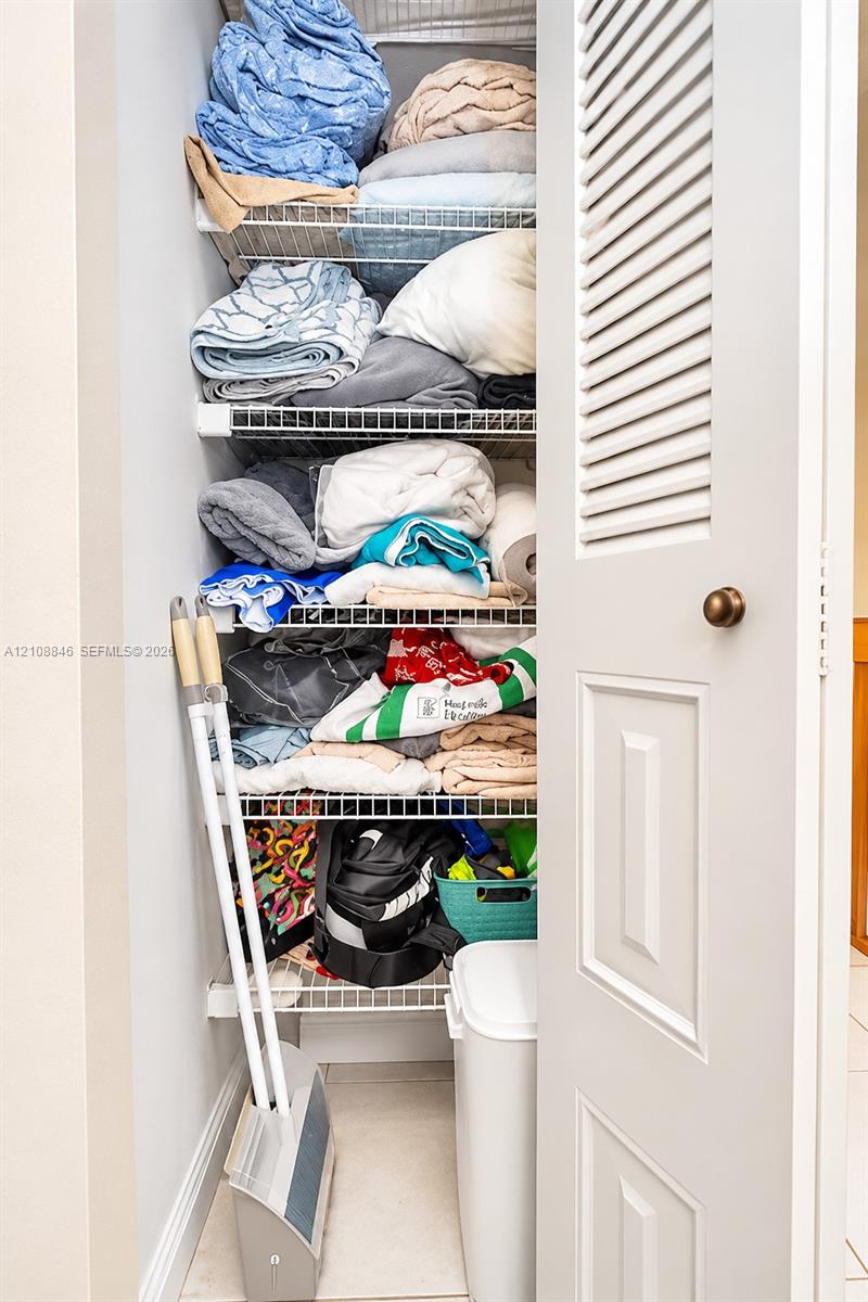 Storage closet featuring white louvered door, brass-finish hardware, and multiple levels of white coated wire shelving