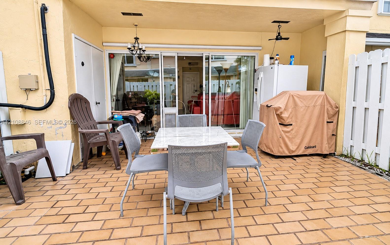 Covered patio featuring brick-style paver flooring, sliding glass doors, built-in storage closet, and white privacy fencing
