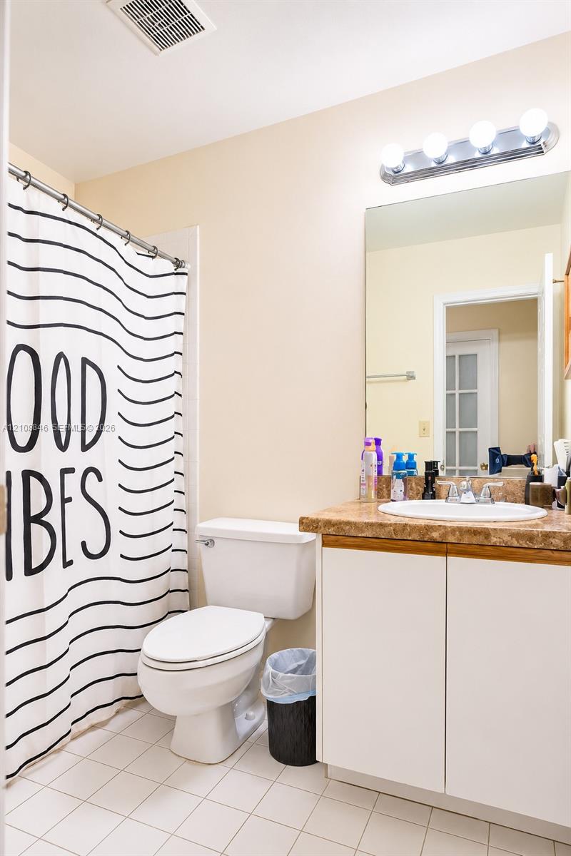Bathroom featuring a vanity with a stone-finish countertop, integrated sink, white cabinetry, wall-mounted four-bulb lighting fixture, and tile flooring