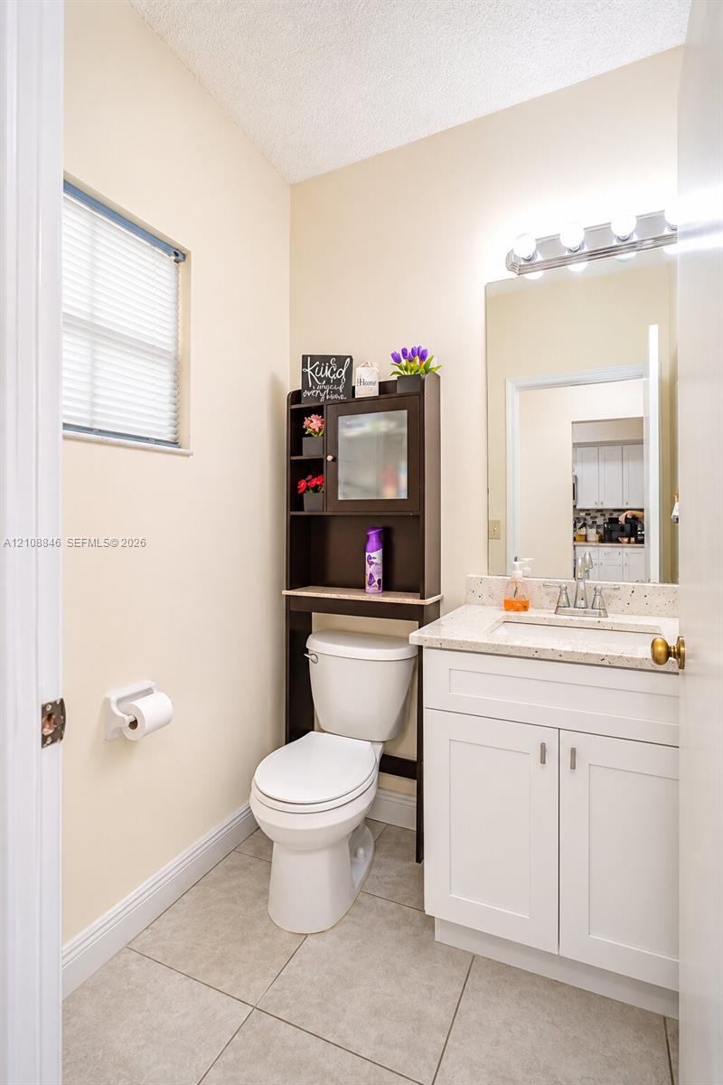 White vanity with stone-composite countertop, undermount sink, ceramic tile flooring, and integrated wall mirror with overhead light fixture