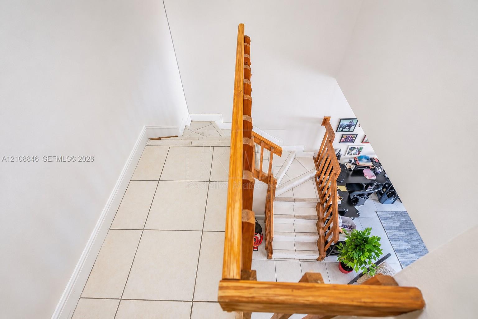 Staircase featuring natural wood-finish railings, tile flooring, and vertical balusters