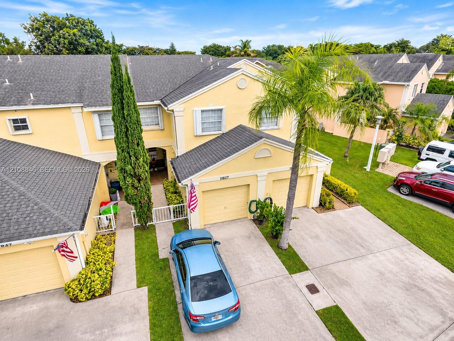 Two-story residence featuring a multi-gabled roofline, stucco exterior, attached two-car garage, concrete driveway, and established palm landscaping