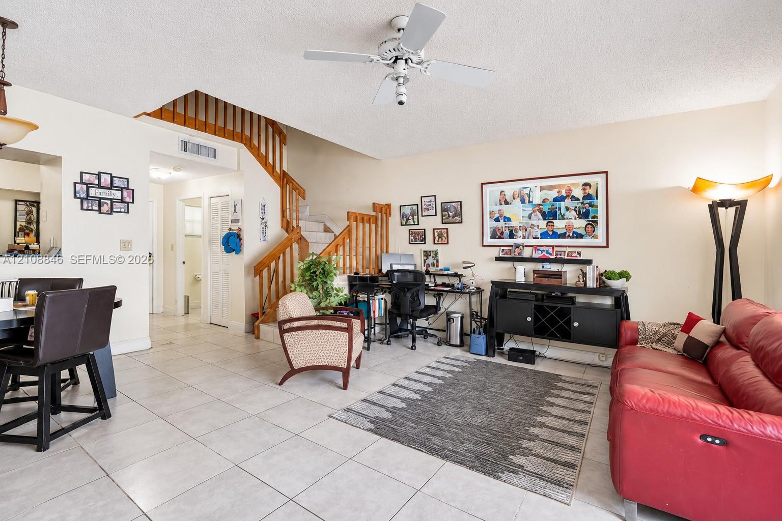 Open-concept living space featuring ceramic tile flooring, a wooden staircase with vertical balusters, and a ceiling fan