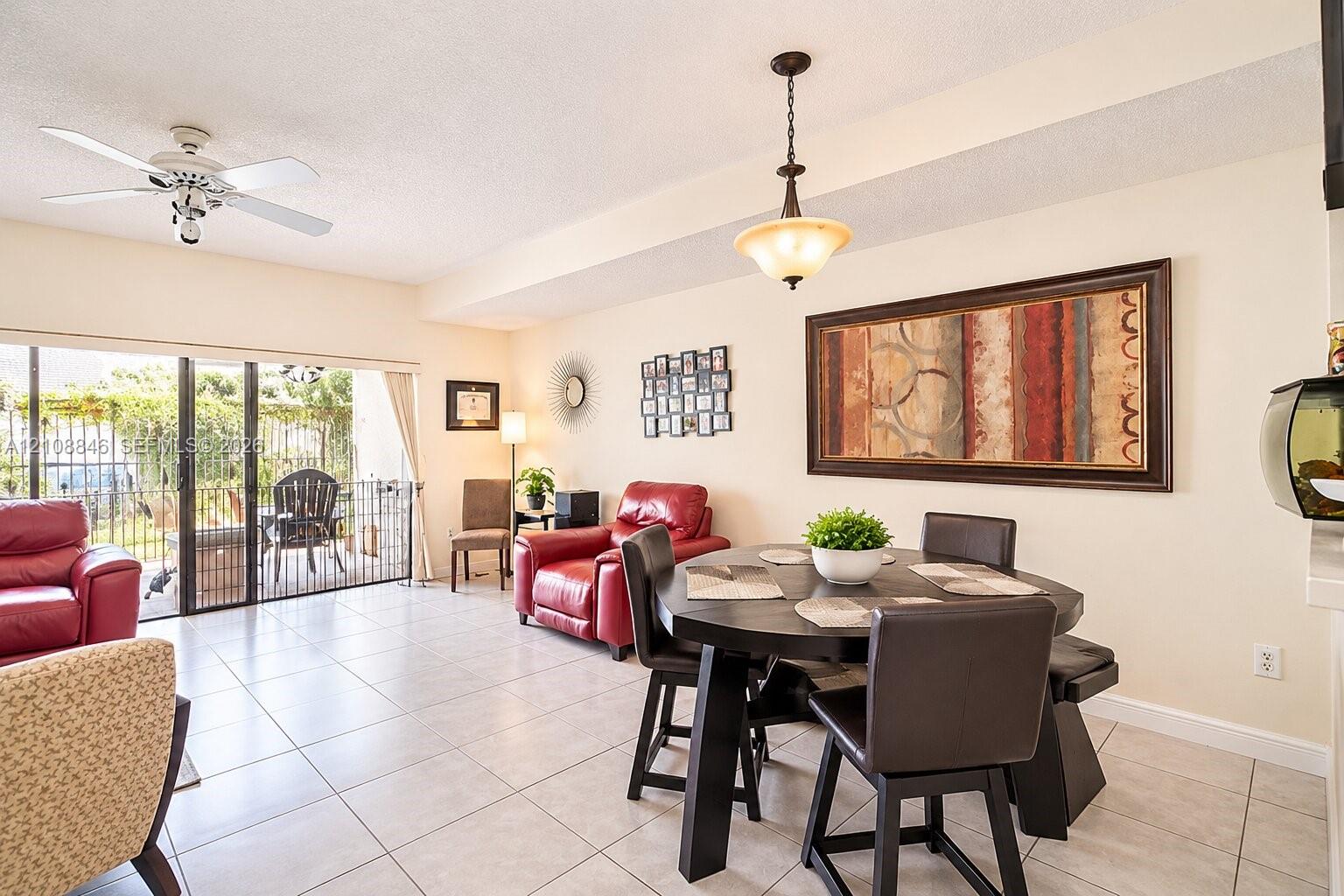 Open living area featuring neutral tile flooring, a ceiling fan with integrated lighting, a bowl-style pendant light fixture, and sliding glass doors