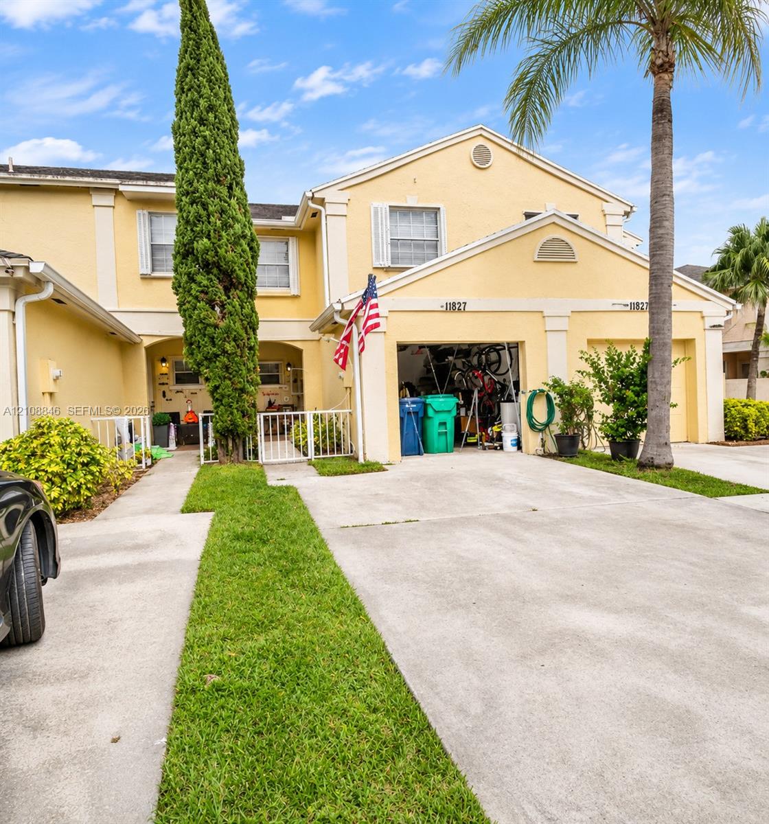 Stucco exterior townhouse featuring a two-car garage, concrete driveway, and front gated courtyard