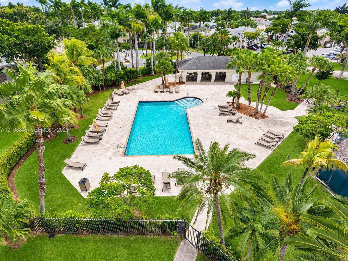 Community swimming pool featuring a stone-paver deck, integrated step entry, shaded pavilion, and surrounding mature landscaping