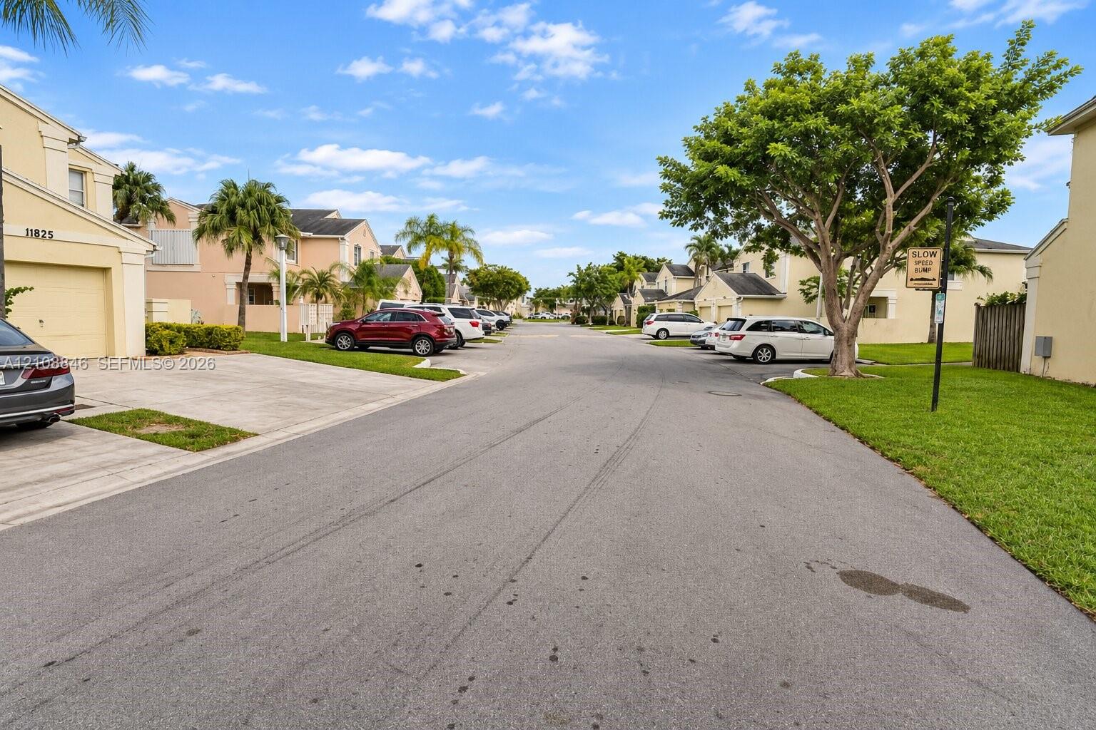 Residential streetscape featuring stucco-finished exteriors, paved driveways, attached garages, and established landscaping with mature palm and broadleaf trees