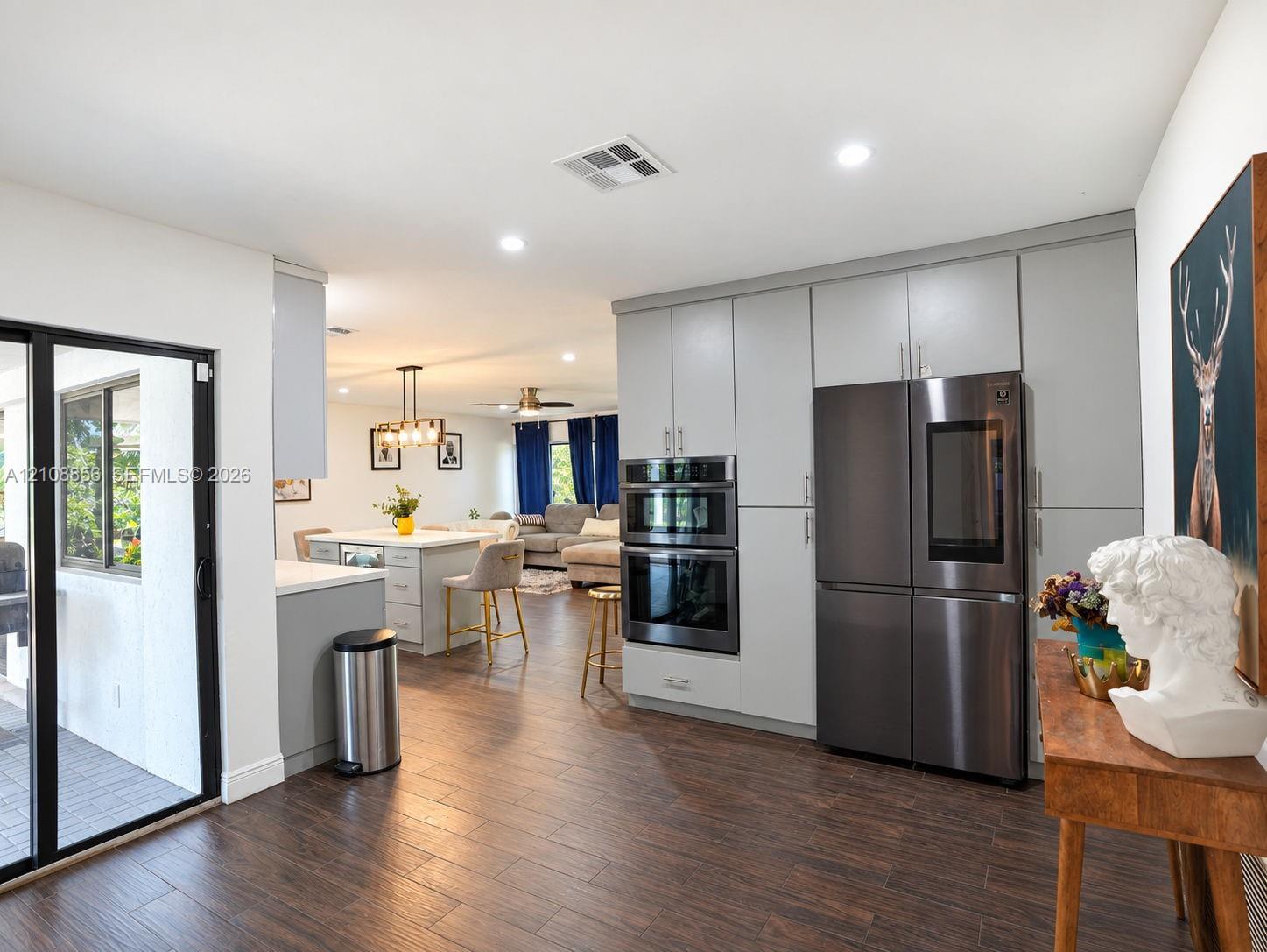 Kitchen featuring full-height light gray cabinetry, built-in stainless steel double wall ovens, a multi-door refrigerator, a center island, and wood-finish flooring