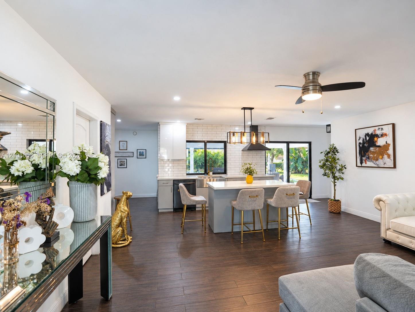Open-concept kitchen featuring an island with stone countertop, white subway tile backsplash, farmhouse-style sink, dark cabinetry, and wood-finish flooring