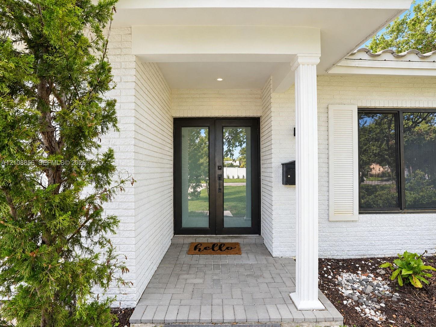 White painted brick exterior featuring a covered entryway with a column, double-glass front doors, and paved stone flooring