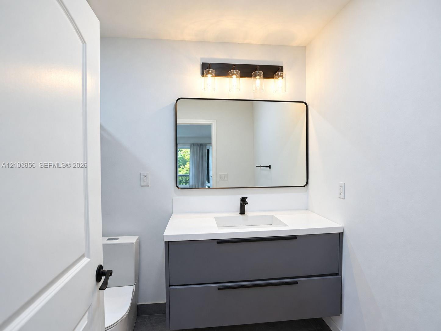 Floating vanity with matte finish charcoal cabinetry, white countertop, rectangular integrated sink, wall-mounted matte black faucet, and rectangular mirror with black frame