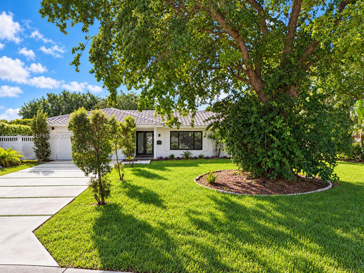 Single-story exterior featuring a light-toned facade, tile roof, concrete paver driveway, and mature landscaping with established trees