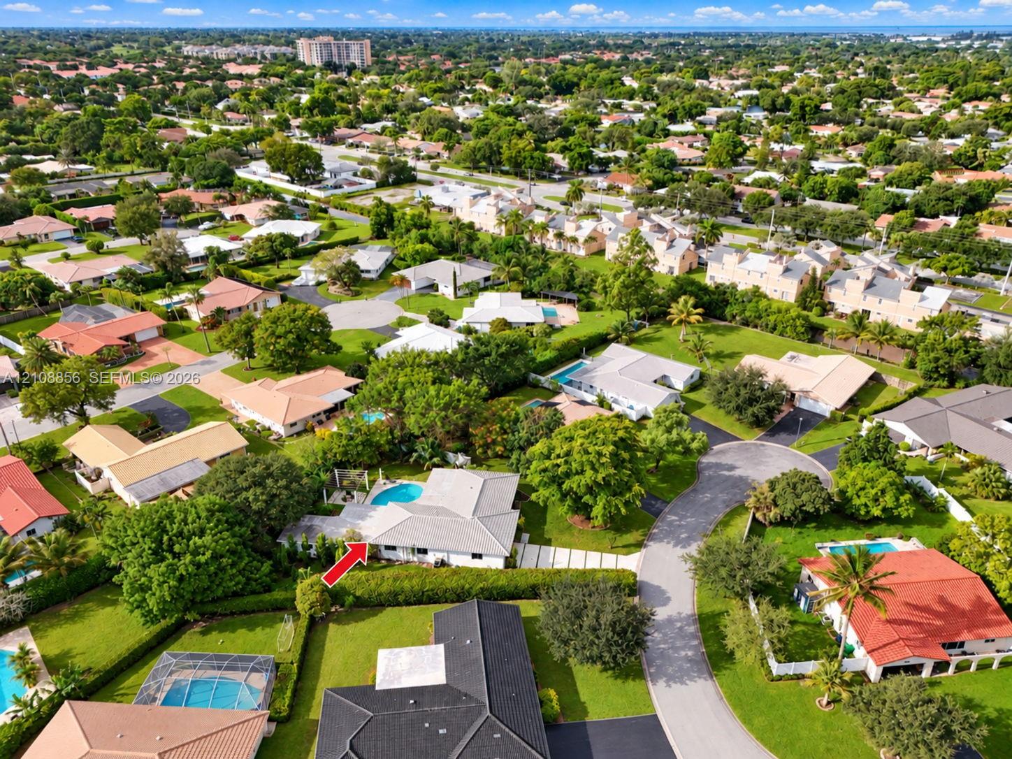 Aerial view of a residential property featuring an outdoor swimming pool, paved driveway, expansive lawn, and mature landscaping