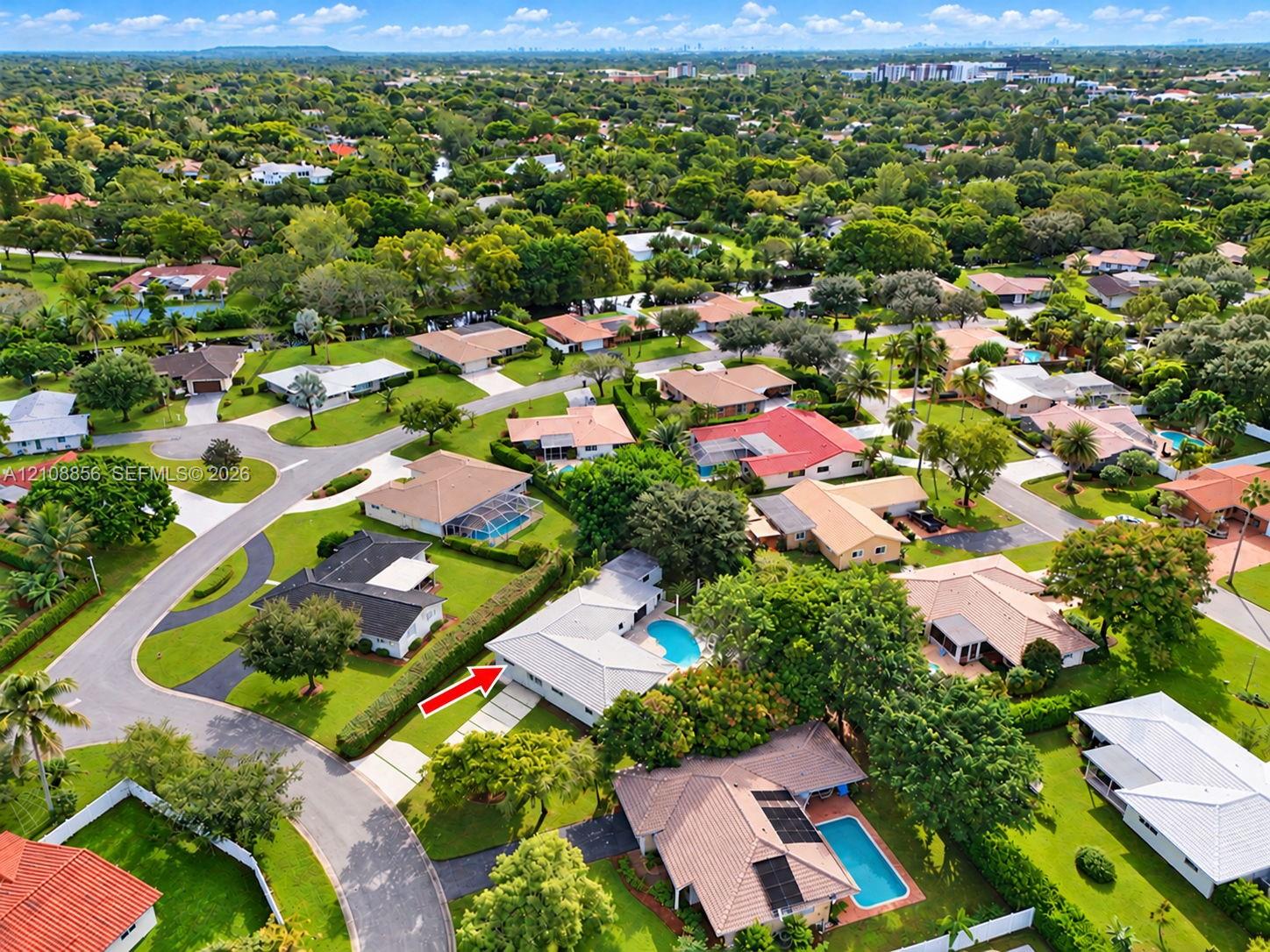 Aerial perspective of a single-story residence featuring a private swimming pool, concrete driveway, and mature landscaping